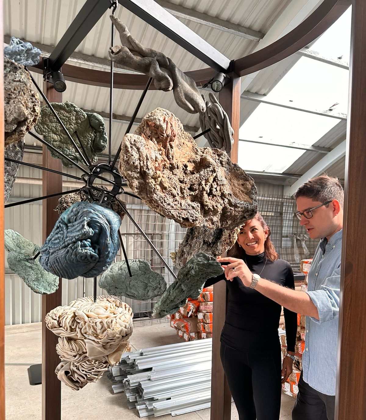 Carolina Sevilla standing beside the suspended installation during its assembly, one hand on the timber post, looking up at the work
